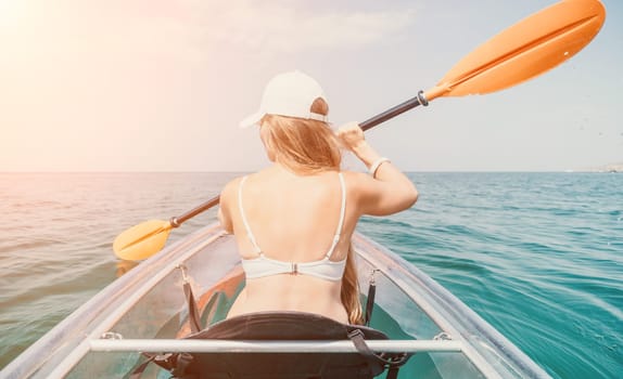 Woman in kayak back view. Happy young woman with long hair floating in transparent kayak on the crystal clear sea. Summer holiday vacation and cheerful female people having fun on the boat.