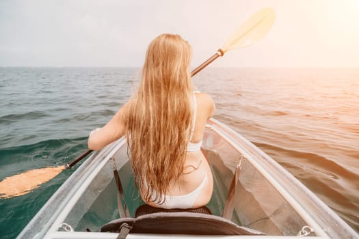 Woman in kayak back view. Happy young woman with long hair floating in transparent kayak on the crystal clear sea. Summer holiday vacation and cheerful female people having fun on the boat.