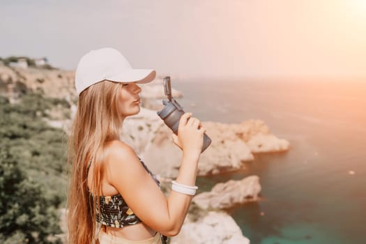 Woman travel sea. Happy tourist taking picture outdoors for memories. Woman traveler looks at the edge of the cliff on the sea bay of mountains, sharing travel adventure journey.