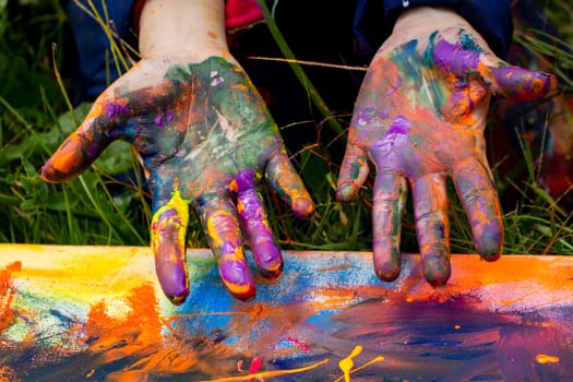 hands full of paint on a freshly painted canvas on the grass. the hands are full of many colors and the author has just finished painting the work