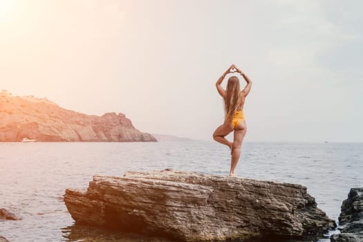 Woman meditating in yoga pose silhouette at the ocean, beach and rock mountains. Motivation and inspirational fit and exercising. Healthy lifestyle outdoors in nature, fitness concept.