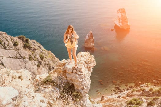 Woman travel sea. Happy tourist taking picture outdoors for memories. Woman traveler looks at the edge of the cliff on the sea bay of mountains, sharing travel adventure journey.