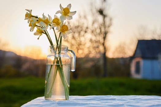 flowers in a vase stand outside during sunset on a table with a white tablecloth. High quality photo