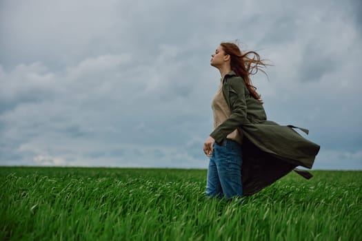 a red-haired woman in a long coat stands in a green field and the wind blows her hair. High quality photo