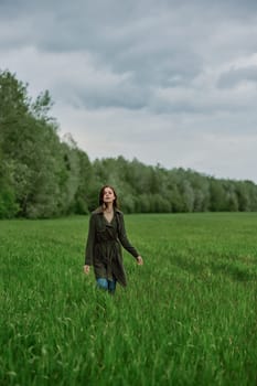 a beautiful woman in a long raincoat runs across a field in high grass in spring in cloudy weather. High quality photo