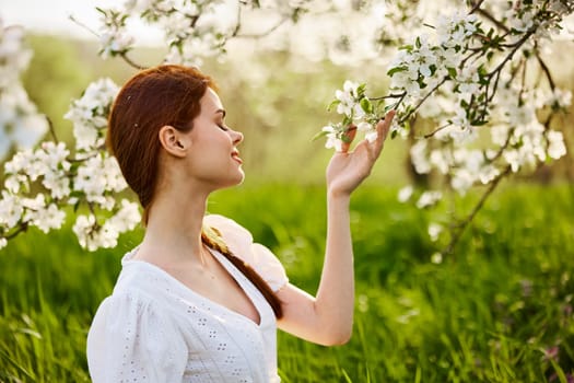 sweet, beautiful woman in a light short dress touches the branches of a flowering tree. High quality photo