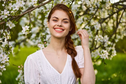 a joyful, carefree woman in a light dress stands against the background of a flowering tree. High quality photo