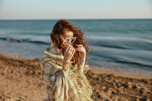 a woman wrapped in a plaid walking along the sea coast straightens her sunglasses. High quality photo