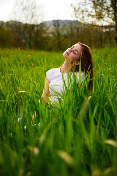 cute, happy woman in white t-shirt midit in green grass. High quality photo