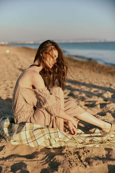 a woman near the sea sits on a blanket and looks into the distance in windy weather. High quality photo