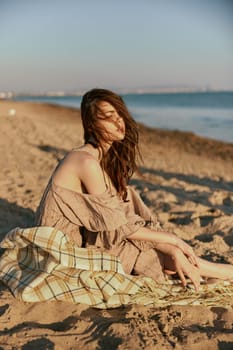 a woman near the sea sits on a blanket and looks into the distance in windy weather. High quality photo