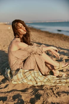 a woman near the sea sits on a blanket and looks into the distance in windy weather. High quality photo