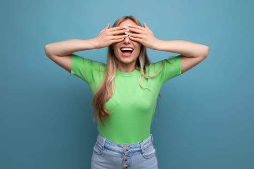 young smiling woman in casual outfit covered her eyes on a blue isolated background.