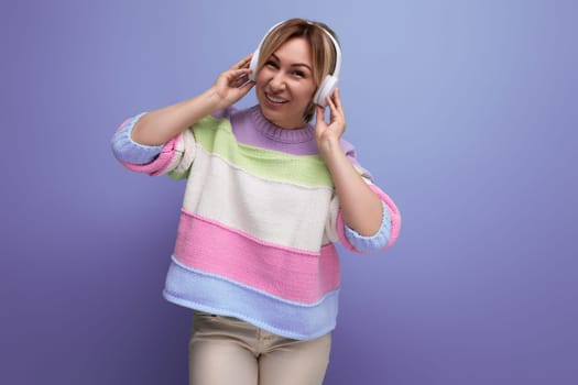 young bright blond girl listens to music in big white headphones on a purple background with copy space.