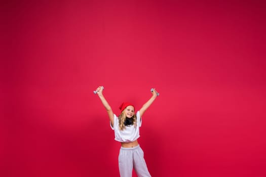 Kid girl doing fitness exercises with dumbbells on a red background