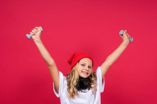 Kid girl doing fitness exercises with dumbbells on a red background