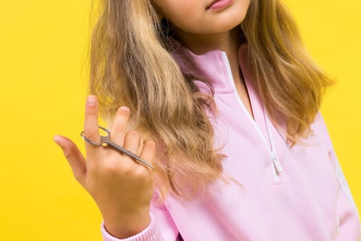 Child adorable girl hairdresser cutting long blonde hair with metallic scissors on a yellow