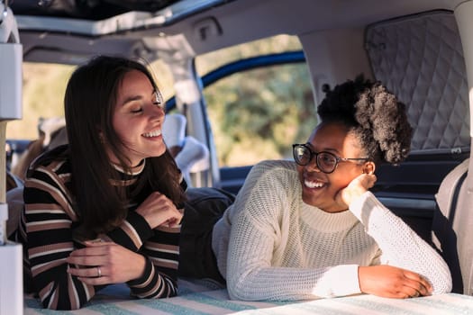 two young women enjoying van life relaxation, concept of weekend getaway with friend and road trip with camper van