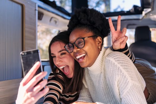 two happy young women having fun taking a selfie photo in a camper van, concept of weekend getaway with best friend and road trip adventure