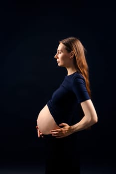 Beautiful pregnant woman over black background. Artistic low key light in studio. High quality photo