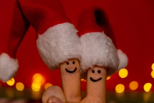 Fingers dressed in Santa-Claus red-white hats. Two happy finger smileys faces representing social network on red background. Copy space for your text Fingers faces in Santa hats against red background. Happy family celebrating concept for Christmas or New Years day. Finger couple Copy space for your text