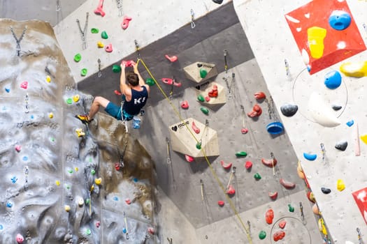 The climber trains on the artificial rock wall with insurance in bouldering gym, April 2022, Prague, Czech Republic.