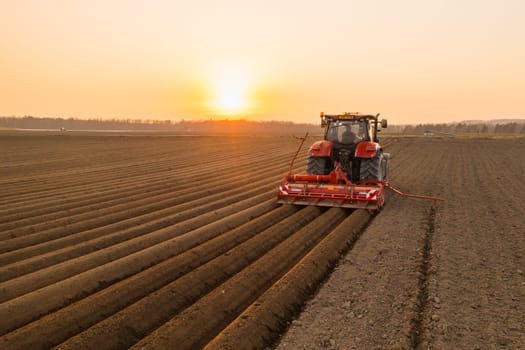 Red tractor working in agricultural field at sunset to avoid a food crisis.
