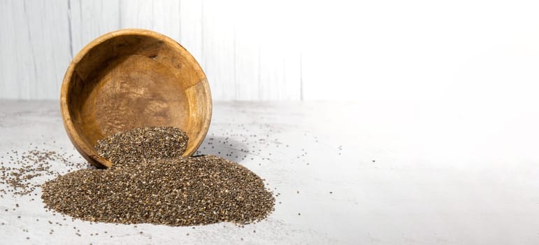 Chia seeds fall from wooden bowl. Healthy superfood rich in Omega 3 fatty acids. Dry healthy natural ingredient. Chia grains are falling. Vegetarian food