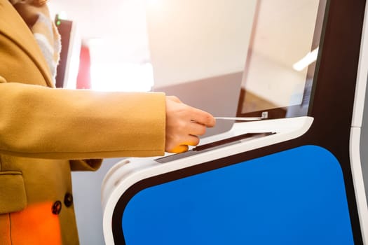 Female passenger scans passport by self service kiosk to check-in for flight and avoids bored queue in international airport terminal close side view