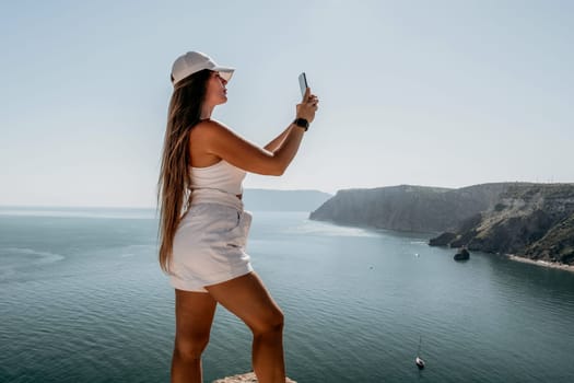 Successful business woman in yellow hat working on laptop by the sea. Pretty lady typing on computer at summer day outdoors. Freelance, travel and holidays concept.