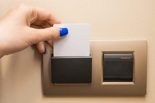 Woman hand puts key card to panel to switch on electricity in hotel room