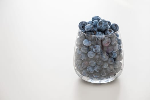 Blueberry in the glass standing on the white table. Healthy snack