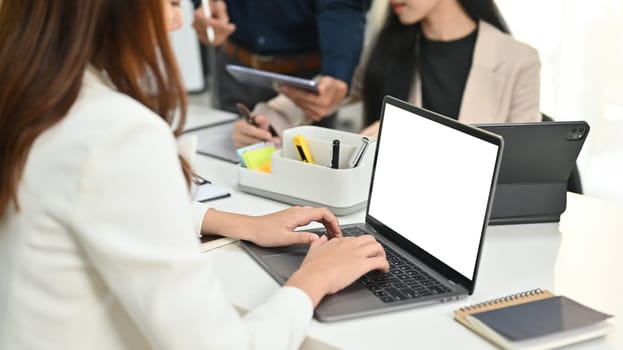 Side view of female employee using laptop computer, sitting at meeting table at modern office.