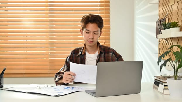Image of asian male in smart casual wears using laptop at home office. Freelance, distance, education, e-learning concept.