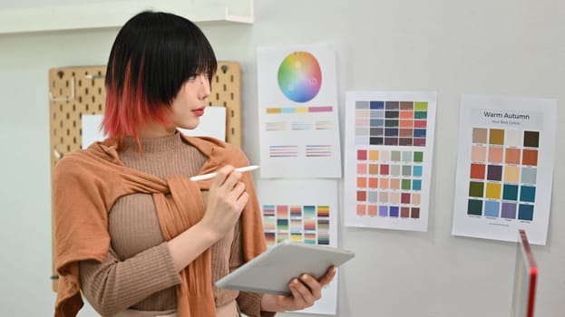 Young asian woman designer illustrator standing in modern design studio and using digital tablet.