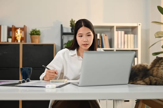 Focused female freelancer in smart casual wears looking at laptop screen, working online or checking email at the morning.