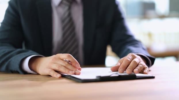 Businessman with pen in hands studying document at table in office closeup. Signing business contract concept