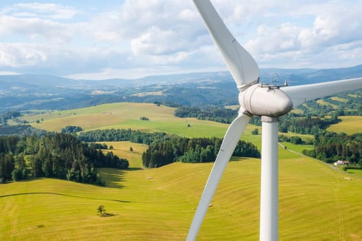 Close up a propeller of a wind turbine in a wind park in the yellow field and mountains in the background in a sunny day. Renewable energy production.