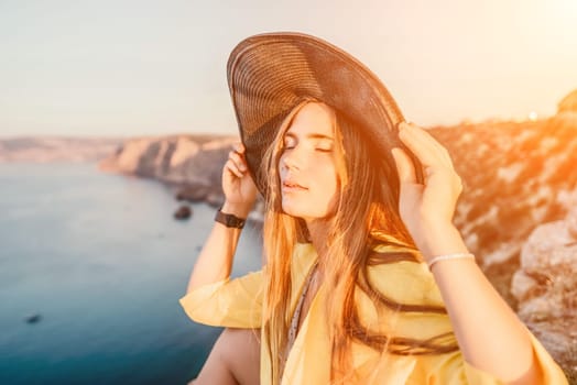 Portrait of happy young woman wearing summer black hat with large brim at beach on sunset. Closeup face of attractive girl with black straw hat. Happy young woman smiling and looking at camera at sea