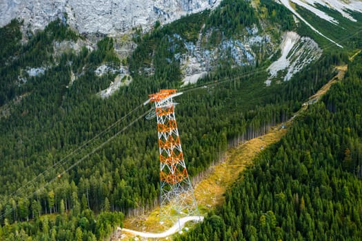 Power line pylon high in the mountains surrounded by trees, aerial view