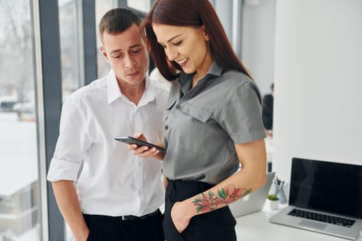 Man with woman using phone. Group of people in official formal clothes that is indoors in the office.