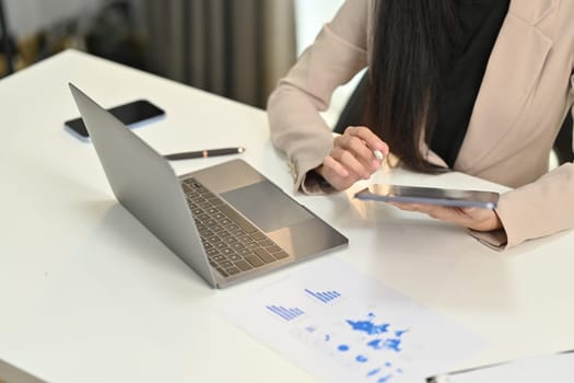 Female accountant using digital tablet and working on bookkeeping documents, checking financial data at office.