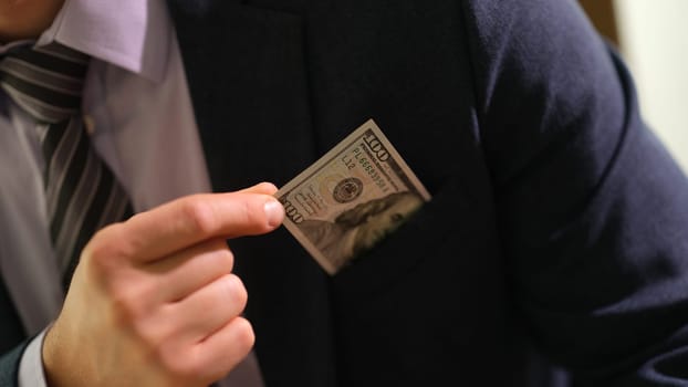 Businessman in business suit pulling out hundred dollar bill from pocket closeup. Bribery and black bookkeeping concept
