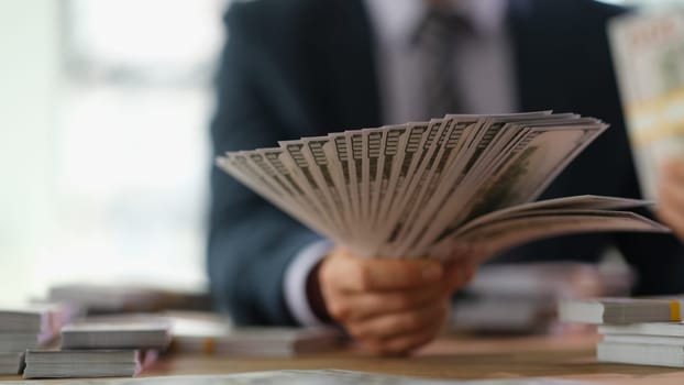 Businessman holding fan of money 100 dollar bills in office closeup. Successful financial transactions concept