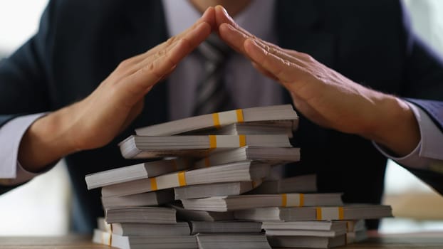 Businessman making roof from hands over bunch of money bundles closeup. Reliable holding of money in bank concept