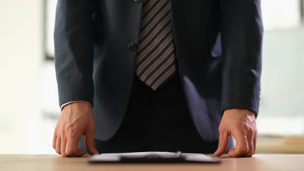 Businessman in suit standing near table with documents at work in office closeup. Control accounting concept