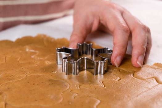 Close up woman hands cutting out cookies with metal mold from the shortcrust pastry. A metal forms in the form of snowflakes for making gingerbread for Christmas.