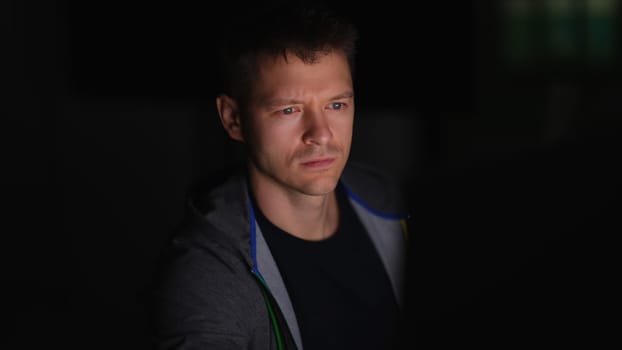 Young man sitting at computer monitor at night. Evening work online concept