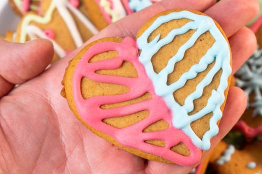 Man holding a heart shaped sugar cookies for St Valentines Day with colorful icing.