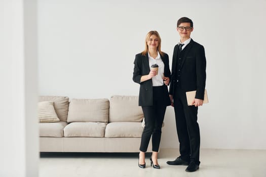 Young guys standing with woman indoors near sofa agaist white wall.